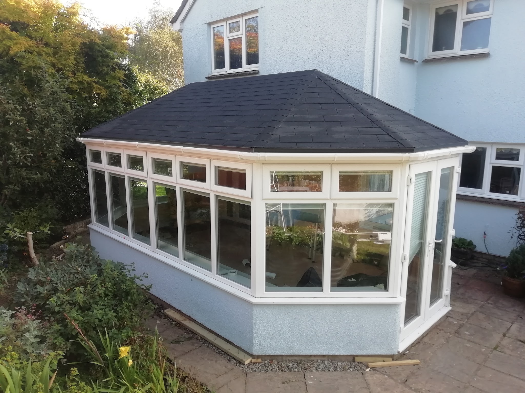 A conservatory with a solid grey tiled roof on a white rendered house