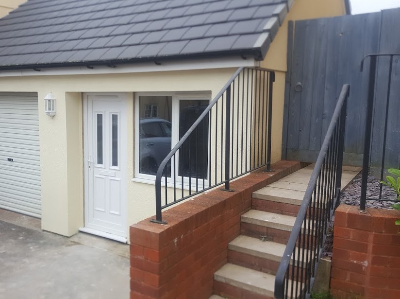 Garage with a roller door, a white front door and brick steps with black railings