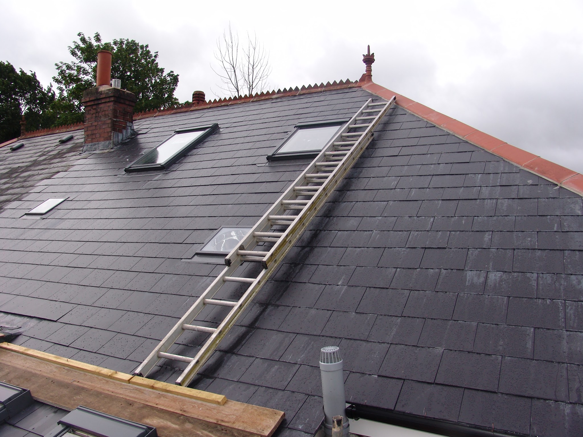 Slate roof with new roof windows fitted and a ladder laid on the roof