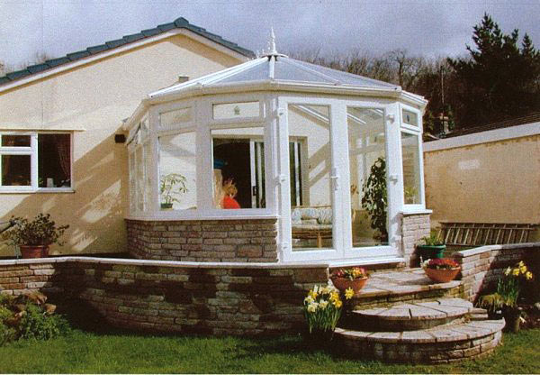 Finished white conservatory on a stone base with daffodils in front