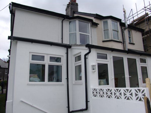A rendered rear extension with white windows and doors on a two-storey house