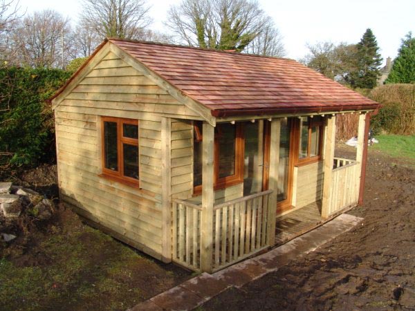 A finished waney-edge timber garden room with a cedar shingle roof and a veranda