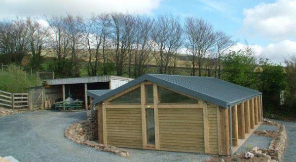 Timber-clad studio building with an oak-framed gable beside a gravel yard